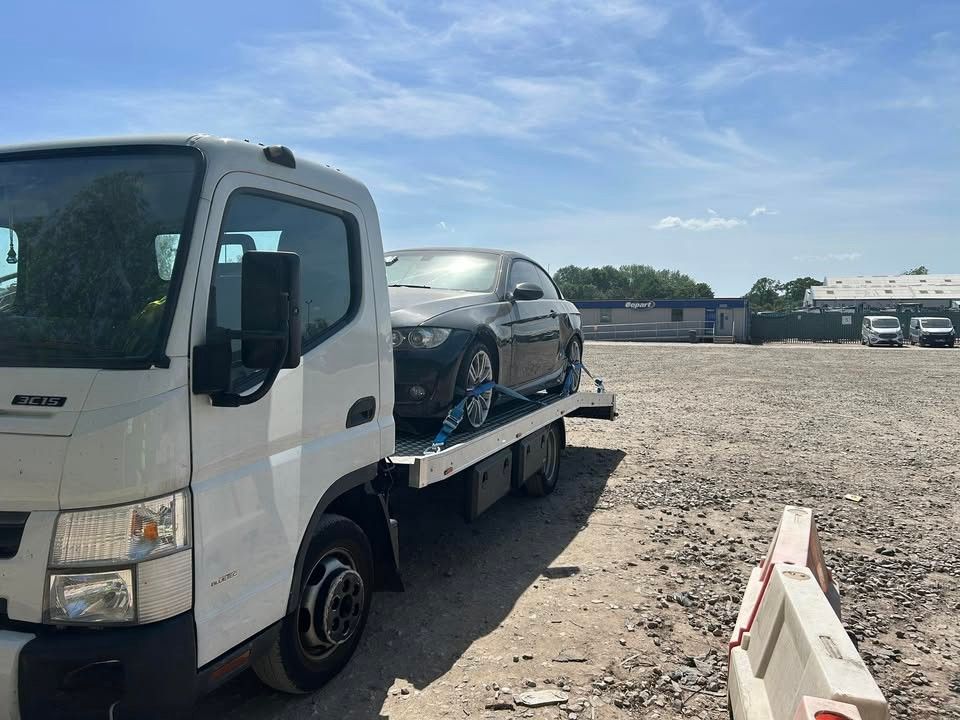 Coupe on a recovery truck at a vehicle yard under blue sky