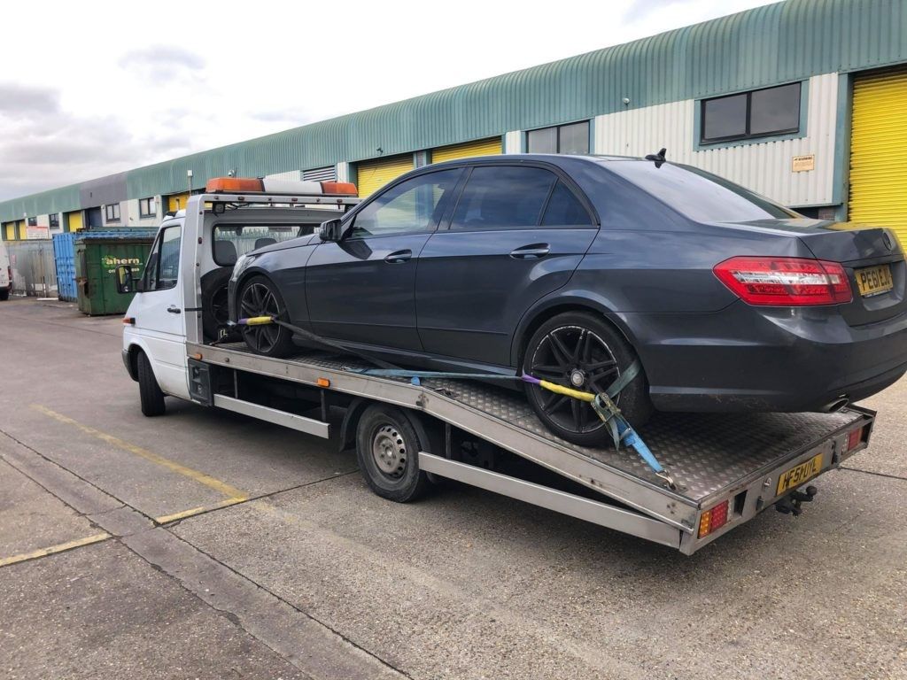 Dark grey saloon strapped securely onto an LDS recovery truck bed outside industrial units