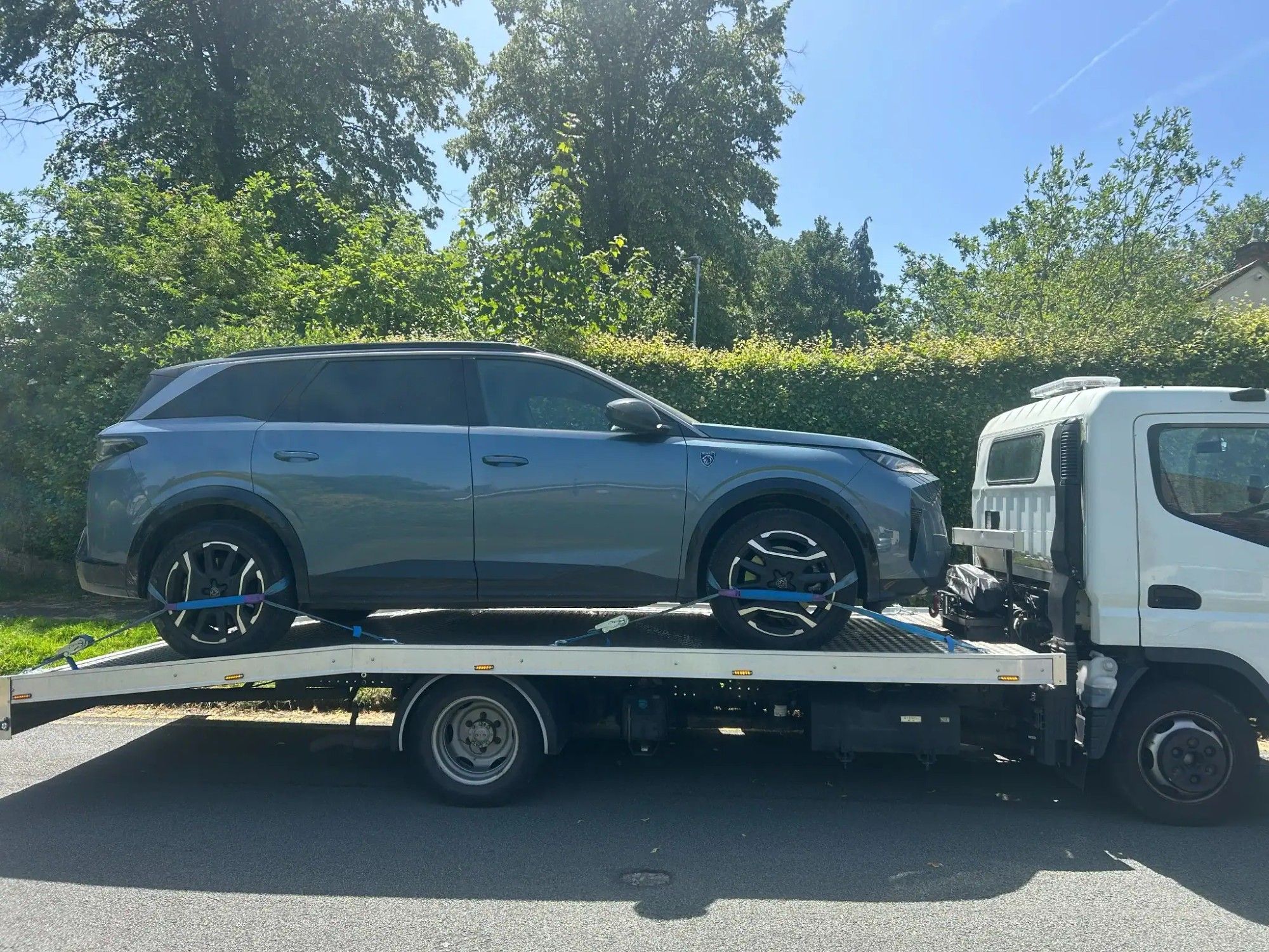 Blue SUV strapped down on the flatbed of a white recovery truck on a residential street